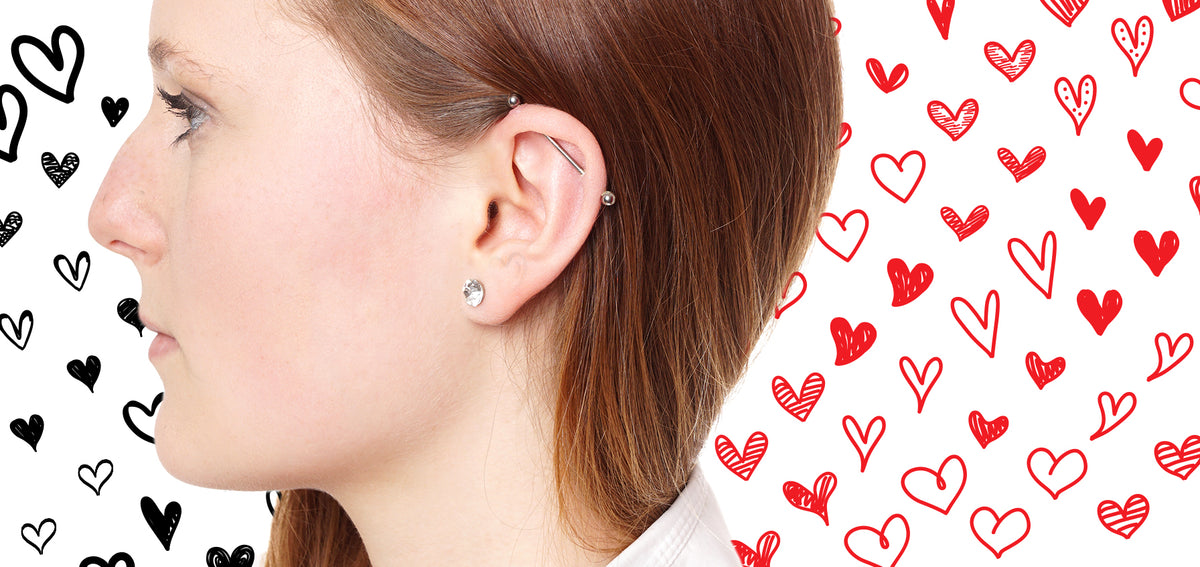 Woman in profile with an industrial barbell across her upper ear and a crystal lobe stud, against hand-drawn hearts