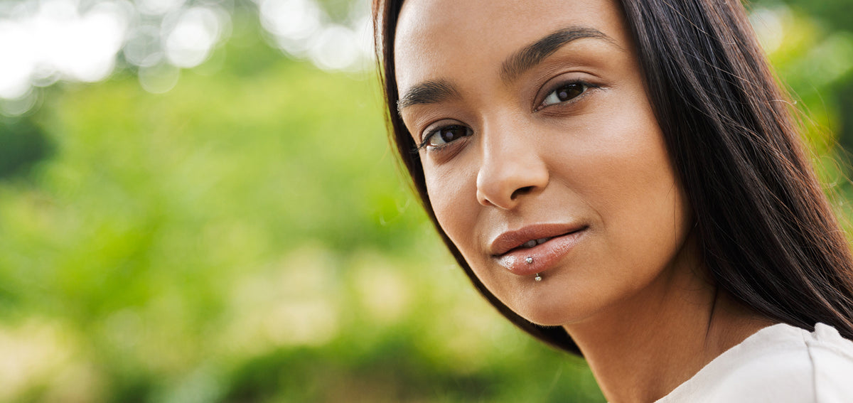 Woman with long dark hair outdoors, wearing a vertical labret with a small bead on her lower lip