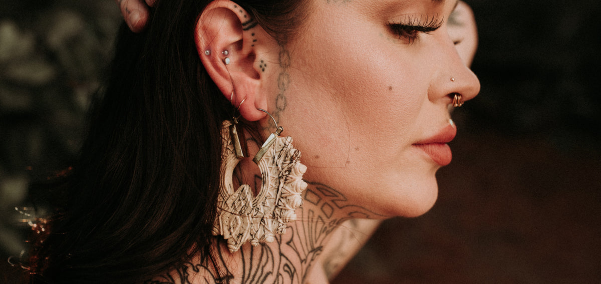 Woman in profile with cartilage studs, thin lobe hoops, a large carved cream ear weight and a nostril stud