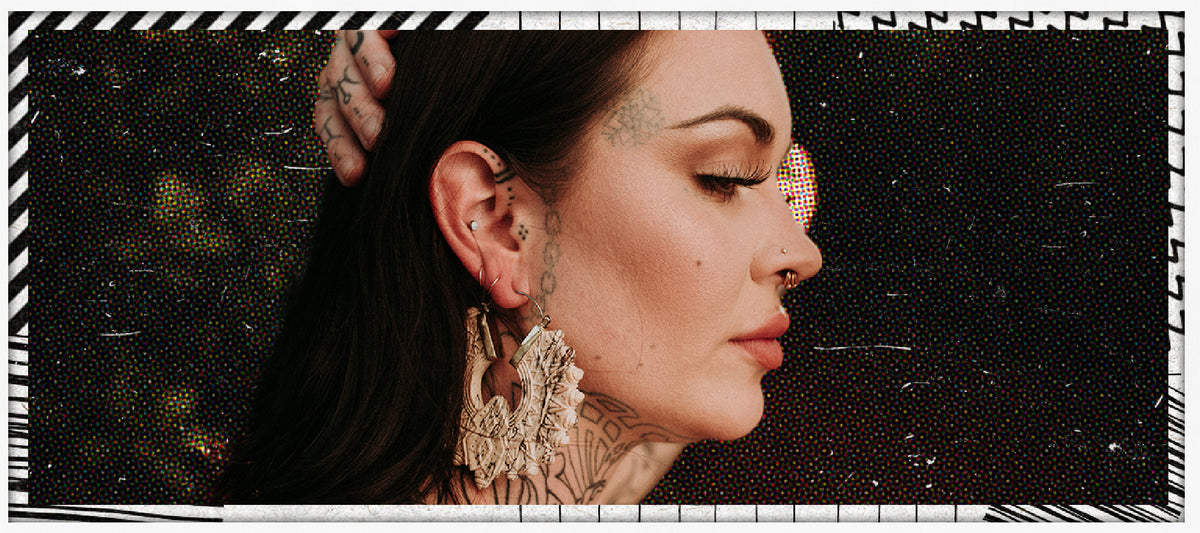 Tattooed woman in profile wearing a carved white ear hanger in a stretched lobe, a nose stud and gold septum ring